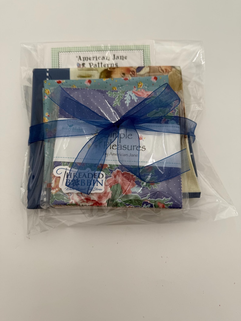 K&ouml;nnte beinhalten: Ein Stoffb&uuml;ndel, verpackt in durchsichtigem Zellophan und mit einem dunkelblauen Band gebunden. Das B&uuml;ndel enth&auml;lt Stoffquadrate mit Blumen- und Tupfenmustern sowie eine Karte mit der Aufschrift "American Jane Patterns" und "Simple Measures".