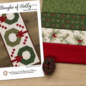 May include: A Boughs of Holly table runner project pattern sheet showing a finished runner with green wreaths and red accents, alongside four folded fabric pieces in green, red, and cream with bird motifs, and a small roll of plaid fabric.