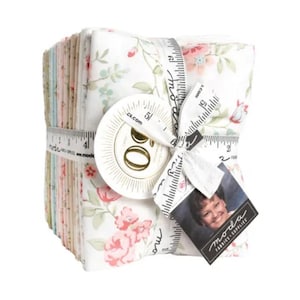 May include: A stack of floral fabric squares tied with a measuring tape ribbon. The fabric features a white background with pink and green floral patterns. A round sticker and a tag with a woman's photo are attached to the ribbon.