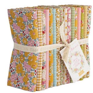 May include: A bundle of floral fabric squares in various colors, including yellow, pink, and green. The fabric is tied with a ribbon that reads "Tilda Quilt Collection." A tag reads "Memories Spring and Early Summer."