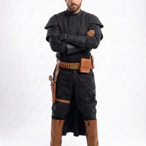 May include: A person wearing a black outfit with a high collar, shoulder pads, and brown leather boots. The outfit includes a utility belt with pouches and a holster. The person has crossed arms and a serious expression.