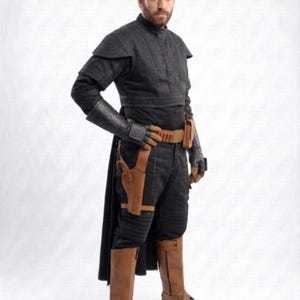 May include: A black costume with a high collar, shoulder pads, and long sleeves. The outfit includes black pants, brown boots, a brown belt, and a holster. The costume has a futuristic or sci-fi aesthetic.