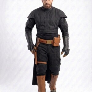 May include: A person in a black outfit with a high collar, shoulder pads, and gloves. The outfit includes black pants, brown boots, and a brown belt with a holster. A small brown pouch is attached to the belt. The person is holding a gun.