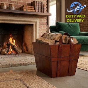 Puede incluir: Un leñero de cuero marrón lleno de leña se encuentra cerca de una chimenea con fuego. El leñero tiene dos asas y está hecho de cuero cosido. El texto "DUTY PAID DELIVERY" es visible en la esquina superior derecha.