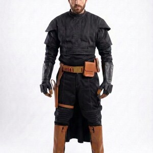 May include: A black costume with brown leather accents. The outfit includes a high-collared top, gloves, a belt with pouches, and brown boots. The costume has a futuristic or fantasy theme.