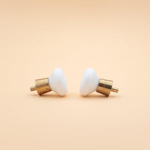 May include: Two white ceramic cabinet knobs with brass fittings. The knobs have a rounded, teardrop shape and are set against a light peach background. Suitable for furniture restoration or DIY projects.
