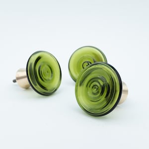 Op de afbeelding: Drie groene glazen kastknoppen met een spiraalvormig ontwerp. De knoppen hebben een messing basis en staan tegen een witte achtergrond. De knoppen zijn een decoratief element voor meubels.