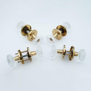 Könnte beinhalten: Vier Vintage-Türknöpfe mit ovalen Griffen aus transparentem, strukturiertem Glas und Messingfarbener Metallbeschläge. Die Knöpfe sind auf einer weißen Oberfläche angeordnet. Ideal für Heimdekoration und Restaurierungsprojekte.
