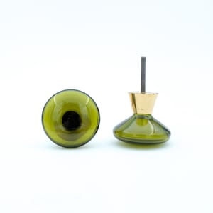 May include: Two olive green glass cabinet knobs with a gold-colored base and a threaded post. One knob is lying on its side, and the other is upright. The knobs are likely for furniture such as drawers or cabinets.