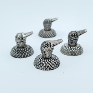 Op de afbeelding: Vier zilverkleurige eendvormige flesstoppers. Elke stopper heeft een gedetailleerde eendenkop en een getextureerd lichaam. De stoppers zijn gerangschikt op een wit oppervlak, wat hun ingewikkelde ontwerp en metallic glans benadrukt.
