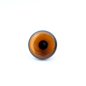 May include: A round, brown bottle stopper with a dark brown rim and a central, dark brown circle. The stopper has a glossy, reflective surface and is set against a white background.
