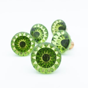 Può includere: Sei pomelli per armadietti in vetro verde con un design sfaccettato. I pomelli hanno un cerchio centrale verde scuro circondato da forme geometriche verde chiaro. I pomelli sono su sfondo bianco.