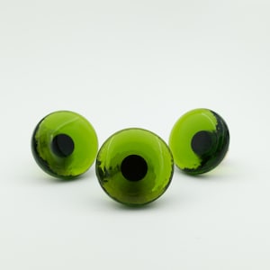 May include: Three round, glass-like cabochons featuring a vibrant lime green outer ring and a solid black circular center. The translucent green material displays subtle variations in color density, creating a smooth, domed surface.