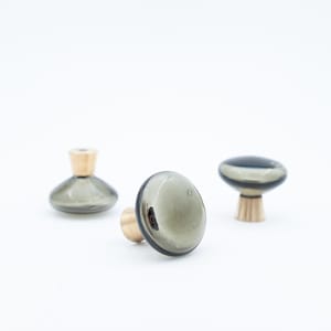 May include: Three decorative cabinet knobs with a smoky gray glass top and a gold-colored base. The knobs have a smooth, rounded shape, and are set against a white background. These knobs are ideal for adding a touch of elegance to furniture.