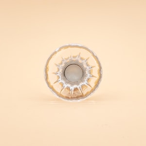Può includere: Un pomello per mobili in vetro trasparente di forma circolare con un motivo sfaccettato a stella che si irradia dal centro. Il pomello presenta un bordo esterno liscio e arrotondato e un punto di fissaggio metallico visibile al centro.