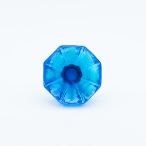 Può includere: Pomello per mobili in vetro blu brillante, di forma ottagonale, con un centro blu scuro. Il pomello ha una superficie strutturata ed è posto su uno sfondo bianco. Ferramenta decorativa.
