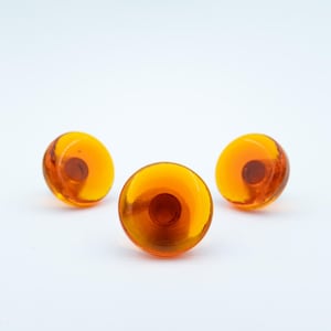 May include: Three circular, translucent amber-colored buttons with a smooth, glossy finish. Each button features a slightly domed surface and a recessed center point, showcasing a vibrant, warm orange hue that catches the light.