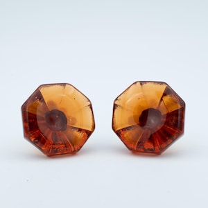 May include: A pair of octagonal amber glass cabinet knobs. Each knob features a dark central element and a faceted design, creating a play of light and shadow. These decorative knobs are ideal for furniture.