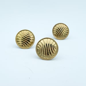 May include: Three gold-coloured, round buttons with a ridged, wave-like design. The buttons are evenly spaced against a white background. The buttons have a shiny, metallic finish.