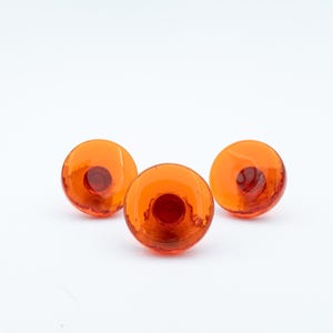 May include: Three circular buttons made of translucent orange glass. Each button features a smooth, domed surface with a recessed center hole for attachment. The buttons are arranged in a triangular formation against a plain white background.