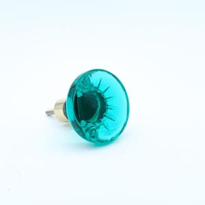 May include: A teal glass cabinet knob with a brass base and screw. The round knob features a starburst design. The hardware is set against a white background.