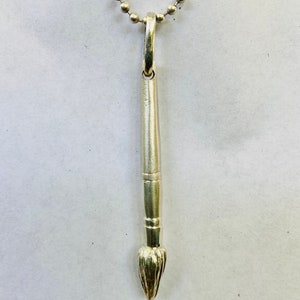 May include: A silver paintbrush pendant necklace. The pendant is shaped like a paintbrush with a detailed brush tip. The necklace is made of a silver chain.