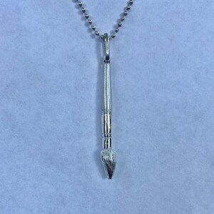 May include: A silver paintbrush pendant necklace with a silver chain.
