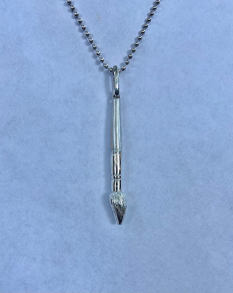 May include: A silver paintbrush pendant necklace with a silver chain.