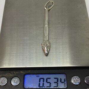 May include: A silver paintbrush charm pendant weighing 0.534 ounces.
