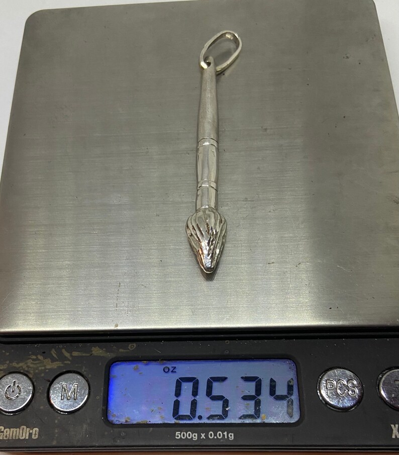 May include: A silver paintbrush charm pendant weighing 0.534 ounces.