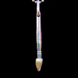 May include: A silver paintbrush pendant necklace. The brush is detailed with a textured bristle tip and a smooth, cylindrical handle.