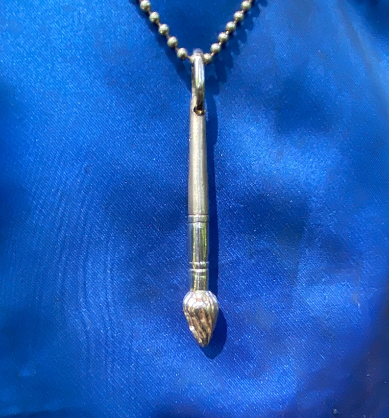 May include: A silver paintbrush pendant necklace on a silver chain. The paintbrush is detailed with a textured brush head.