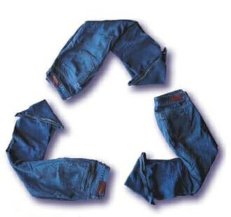 May include: Three pairs of blue denim jeans arranged in a triangular recycling symbol shape. Each pair of jeans is folded to form one of the three segments of the loop, showcasing the dark blue fabric, waistbands, and back pockets of the denim.
