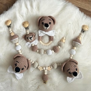 Può includere: Un set di tre morsi per bambini a forma di orsacchiotto in crochet con perline e anelli in legno. I morsi sono beige e marroni con fiocchi bianchi. Le perline sono beige e bianche. Gli anelli sono in legno.