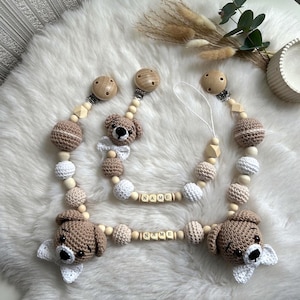Puede incluir: Dos mordedores de bebé de oso de peluche tejidos a crochet con cuentas de madera y bloques de nombre. Los mordedores son de color marrón y crema con detalles blancos. Los bloques de nombre deletrean "NAME".