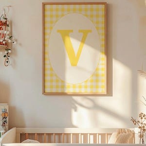 Peut inclure: Une affiche encadrée avec la lettre "V" jaune sur un ovale blanc, sur un fond vichy jaune et blanc. L'œuvre est accrochée au-dessus d'un lit bébé en bois dans une pièce ensoleillée, créant un thème de chambre d'enfant.