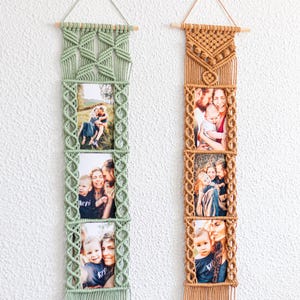 Könnte beinhalten: Zwei Makramee-Foto-Displays hängen an einer weißen Wand. Eines ist salbeigrün, das andere ist hellbraun. Jedes enthält drei gerahmte Fotos. Die Displays bestehen aus geknotetem Kordel und haben oben Holzstäbe zum Aufhängen.