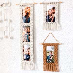 Könnte beinhalten: Makramee-Fotorahmen in Creme und Braun hängen an einer weißen Wand. Die cremefarbenen Halter haben ein rechteckiges Design mit Fransen und halten mehrere Fotos. Der braune Halter hat ein einzelnes Foto und ein dreieckiges Hängedesign.