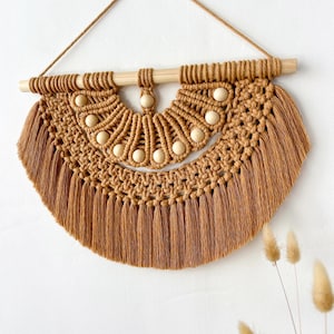 Peut inclure: Suspension murale en macramé marron. Le design en demi-cercle comprend une frange, des perles en bois et une baguette en bois pour la suspension. Cette décoration de style bohème apporte une touche de texture naturelle et un aspect chaleureux.