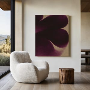 May include: A contemporary living room with a large abstract painting in deep purple hues. A white, plush armchair is placed near a natural wood stump side table. Large windows provide a view of the landscape.