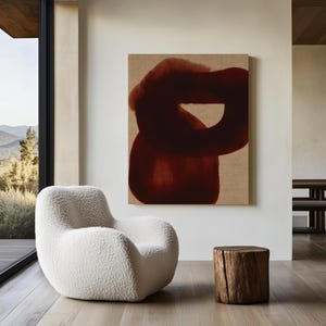May include: A modern living room featuring a white, plush armchair, a small wooden side table, and a large abstract painting with a dark red design. The room has large windows with a view of a mountain landscape.