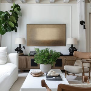 A bright, airy living room with white walls, natural wood accents, and soft neutral furniture creates a fresh and inviting feel. A large indoor plant and modern lighting add warmth and balance. The Samsung Frame TV features soft beige and earth-toned layers with a diffused central form and subtle textured surface. Designed for Frame TV, this neutral artwork creates a calm, gallery-style presence on a television, blending naturally into modern, Japandi, and minimalist interiors.