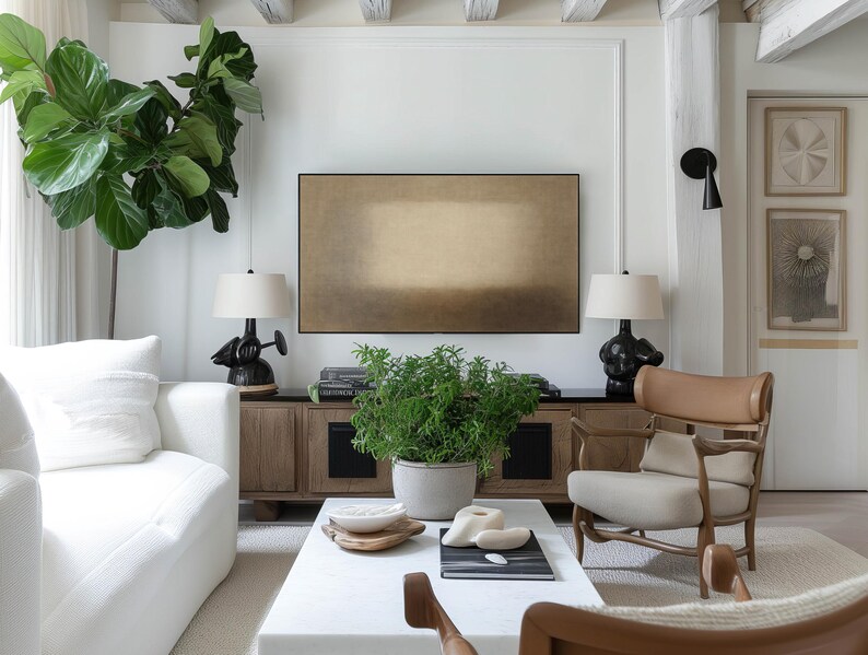A bright, airy living room with white walls, natural wood accents, and soft neutral furniture creates a fresh and inviting feel. A large indoor plant and modern lighting add warmth and balance. The Samsung Frame TV features soft beige and earth-toned layers with a diffused central form and subtle textured surface. Designed for Frame TV, this neutral artwork creates a calm, gallery-style presence on a television, blending naturally into modern, Japandi, and minimalist interiors.