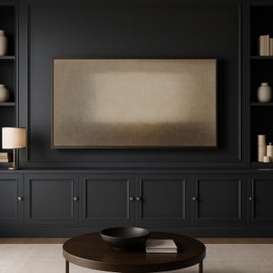 A contemporary living room features dark built-in cabinetry with brass accents, soft ambient lighting, and a clean wood coffee table centered in the space. Mounted on the dark wall, a Frame TV featuring soft beige and earth-toned layers with a diffused central form and subtle textured surface. Designed for Frame TV, this neutral artwork creates a calm, gallery-style presence on a television, blending naturally into modern, Japandi, and minimalist interiors.