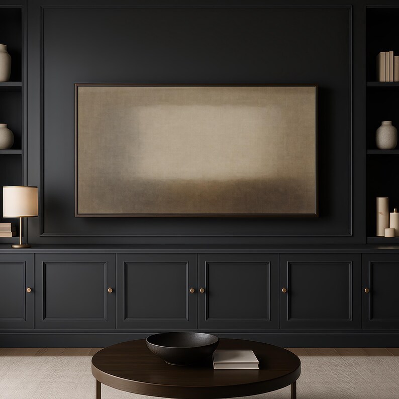 A contemporary living room features dark built-in cabinetry with brass accents, soft ambient lighting, and a clean wood coffee table centered in the space. Mounted on the dark wall, a Frame TV featuring soft beige and earth-toned layers with a diffused central form and subtle textured surface. Designed for Frame TV, this neutral artwork creates a calm, gallery-style presence on a television, blending naturally into modern, Japandi, and minimalist interiors.