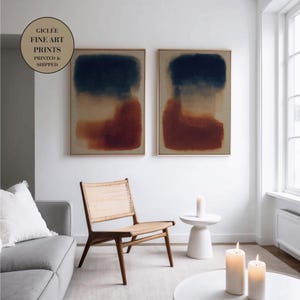 May include: Two rectangular wall art prints featuring abstract color blocks of deep navy blue and burnt orange on a neutral beige background, displayed in thin light wood frames. A circular badge in the corner reads GICLEE FINE ART PRINTS PRINTED & SHIPPED.