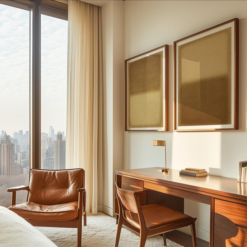 A refined bedroom workspace with mid-century wood furniture, a caramel leather chair, and a large window overlooking the city skyline. Warm morning light filters through sheer curtains, highlighting the Amber & Dawn Divide Set. The two abstract prints in soft ochre and golden brown tones add calm sophistication to the serene interior, harmonizing with the natural textures and minimalist decor.
