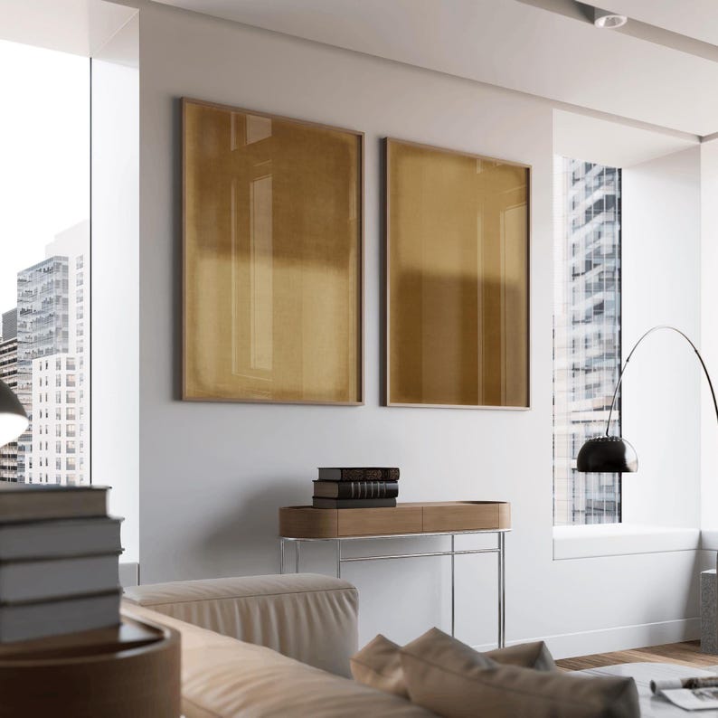 A contemporary high-rise living room with floor-to-ceiling windows, sleek furniture, and cityscape views. The neutral palette and modern decor create a calm, airy space accented by the Amber & Dawn Divide Set. The diptych’s warm amber and golden brown gradients on linen bring organic contrast to the urban setting, softening the minimalist architecture with natural tone and balance.