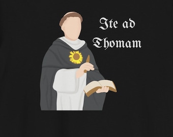 Pode incluir: Camiseta preta com uma ilustração de desenho animado de um homem segurando um livro e um girassol. O texto "Ite ad Thomam" está impresso na camiseta.