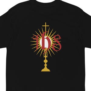 Może przedstawiać: Czarny T-shirt z grafiką przedstawiającą monstrancję w kolorze złotym i czerwonym z literami IHS.